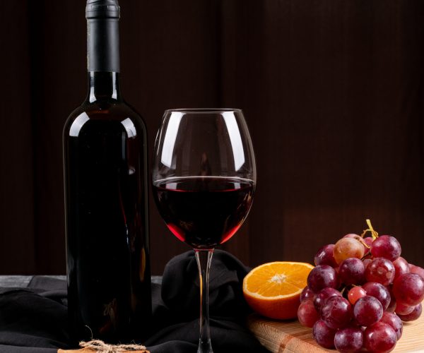 side-view-red-wine-with-grape-orange-wooden-cutting-board-dark-vertical